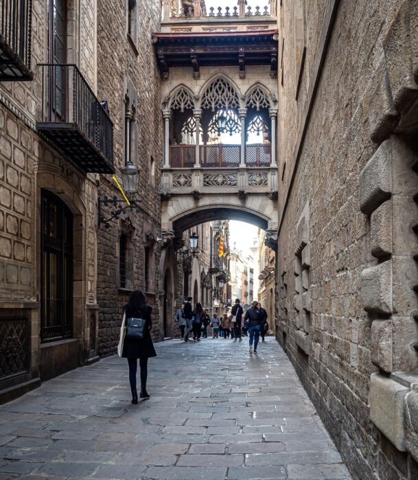 A Woman Walking Down the Streets and Alleys of the Gothic Quarter Barcelona, behind a few groups of fellow tourists and nearby the Barcelona Cathedral