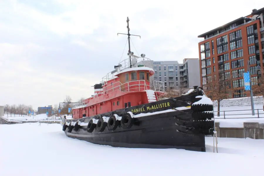 A red and black ship with the name "Daniel McAllister" stationed at the old port of Montreal in the winter, surrounded by snow and ice, perfect for a Montreal free walking tour!