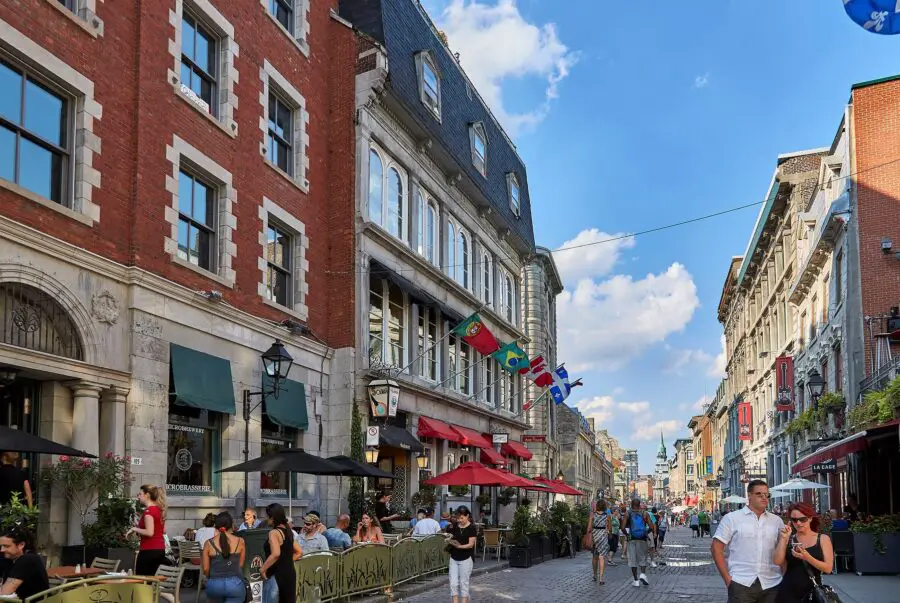 The charming pedestrian streets and buildings' exterior of Old Montreal in the summer, perfect for Montreal solo travel, with some travelers walking on the cobble-stoned streets