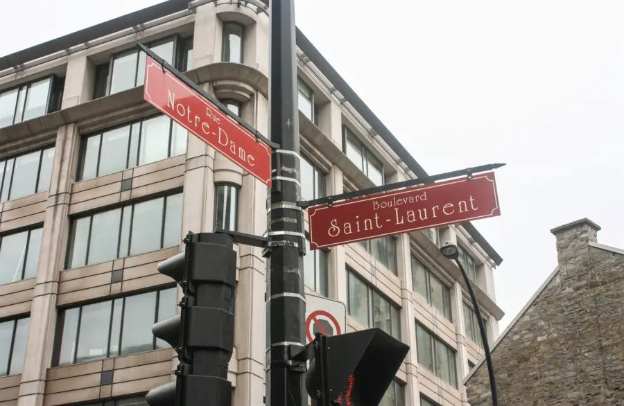 The red street signs at a intersection at the Boulevard Saint-Laurent, a stop on our self-guided Montreal walking tour, including the "Rue Notre-Dame" and "Boulevard Saint-Laurent"
