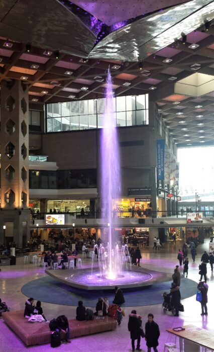 Water spurting out of a small fountain in the Montreal Underground City, lit purple and reaching towards the ceiling