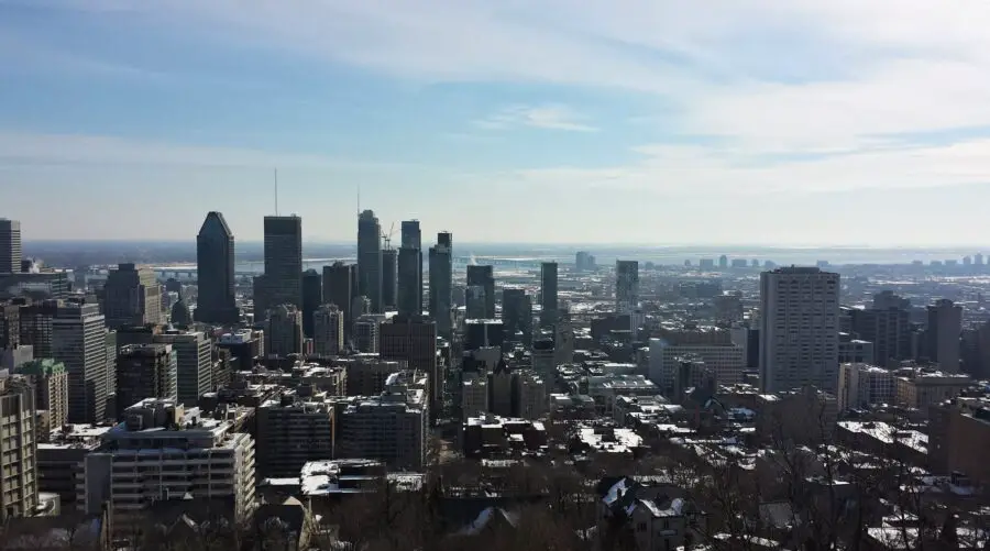 The viewpoint of the Montreal skyline and buildings from Mount Royal Lookout in the winter, with the light sky streaked with white clouds - the first stop on our Montreal walking tour!