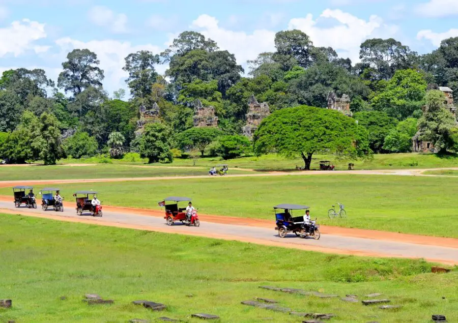 Five tuk tuks driving the roads in Angkor Archeological Park on a bright day, the best way to get from Siem Reap to Angkor Wat