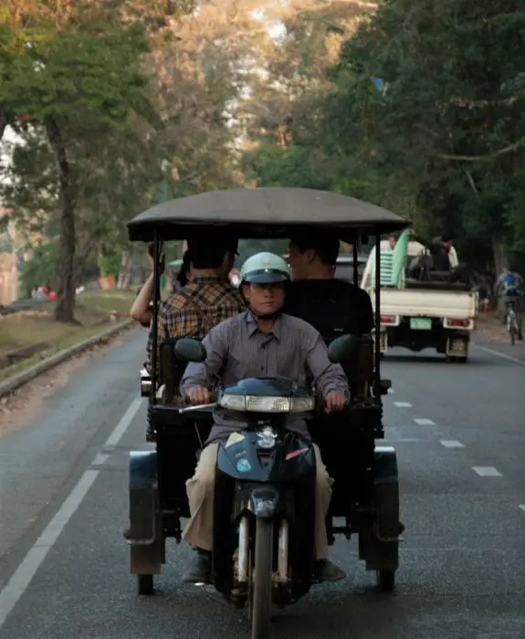 A tuk tuk driver with 3 men in his black cart driving on the roads of Siem Reap, Cambodia