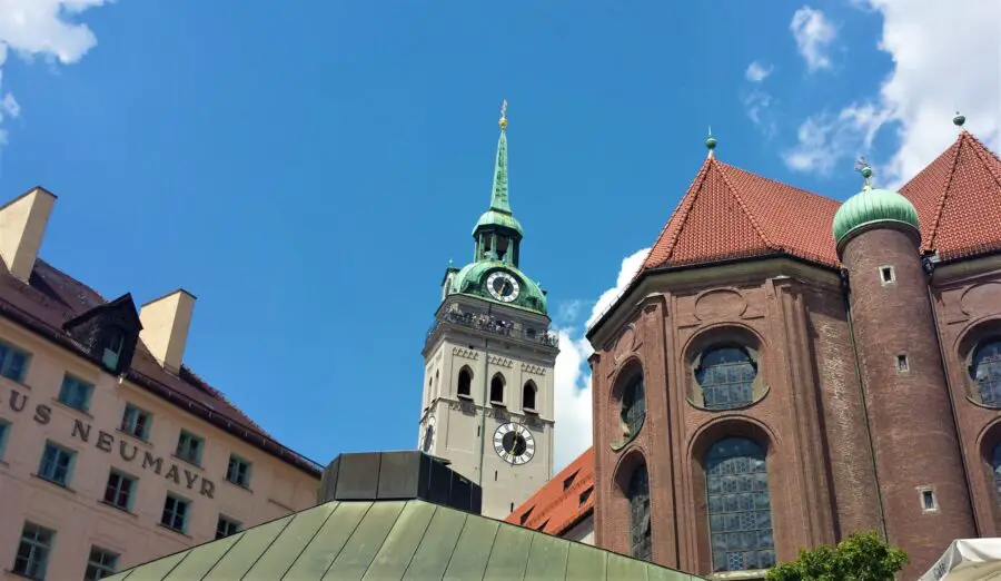 The turquoise tower of St. Peter's Church and its surrounding buildings in Munich on a sunny, bright day