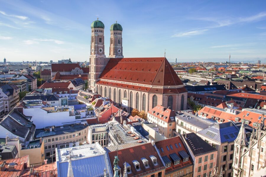 The twin towers of Frauenkirche, with the red roof, grey exterior, and turquoise hoods bathed in sunlight