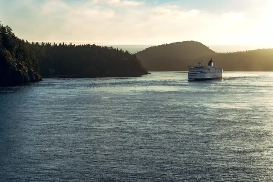 A large, white BC ferry cutting through the calm Pacific Ocean surrounded by dark islands at dusk