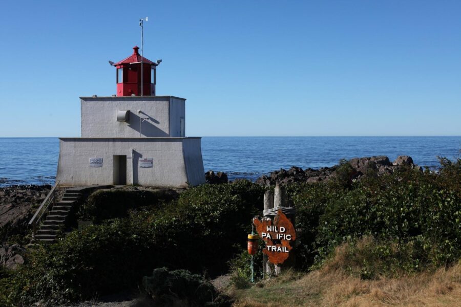A red and grey lighthouse by the calm blue Pacific Ocean on the Wild Pacific Trail, one of the best things to do in Ucluelet