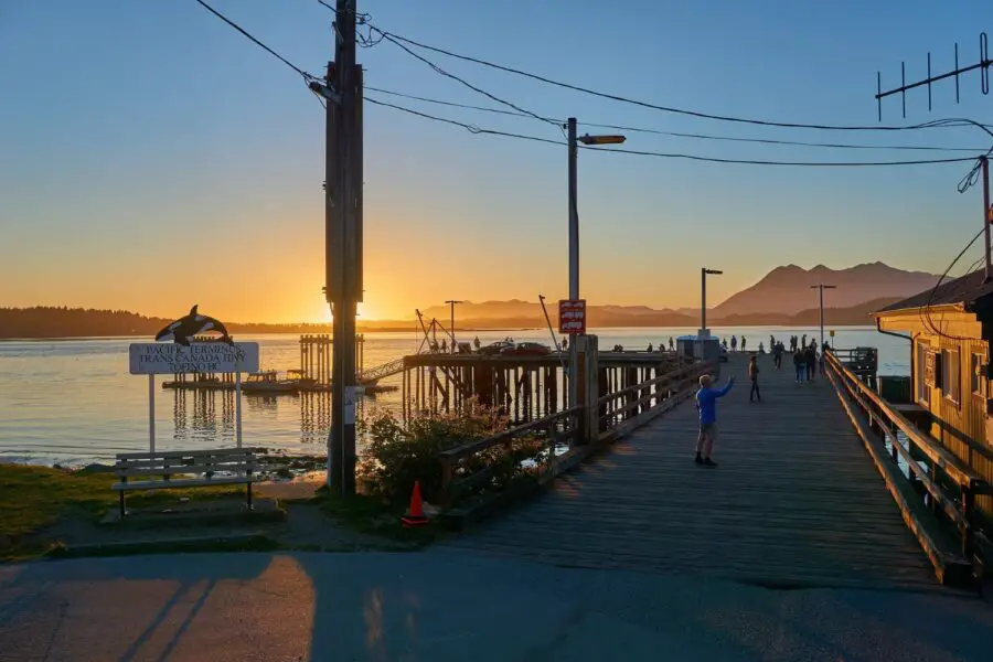 Several people standing on a wooden dock next to the Pacific Ocean at sunset in Tofino British Columbia