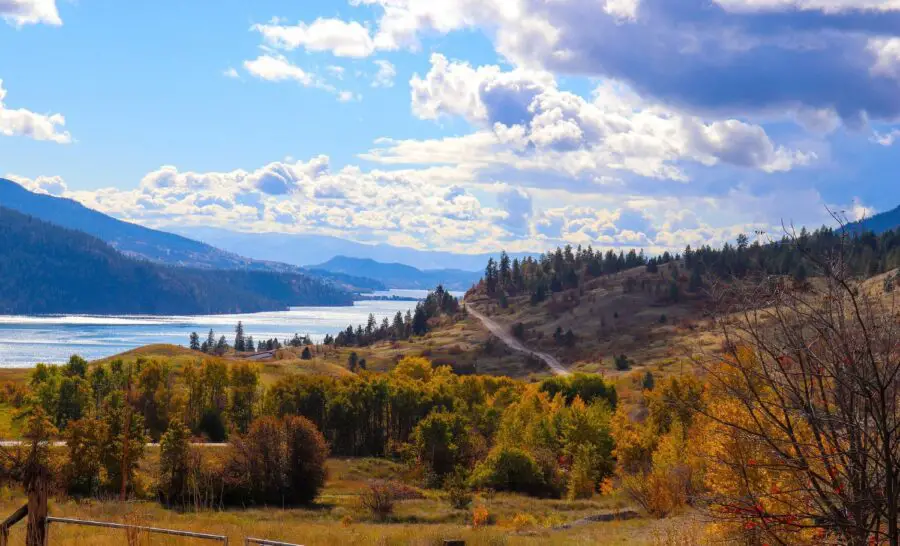 A stunning view of the fall foliage, brown shrubbery, and crystal blue lake in Kelowna BC on a slightly cloudy day