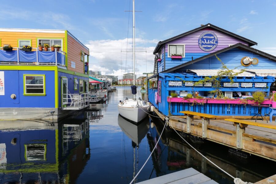 A white boat docked at a blue and purple boutique store in Victoria's Fisherman's Wharf next to some colorful houseboats