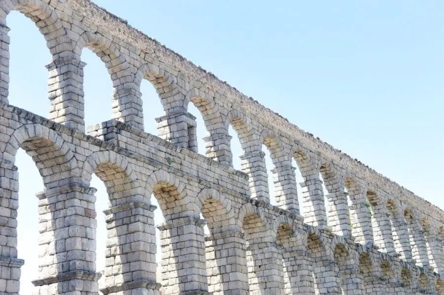 Bright photo of the stone arches of the Segovia Aqueduct on a sunny day.