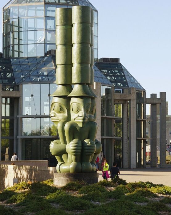 A green First Nations' statue outside of the glass buildings of the Ottawa National Gallery of Canada