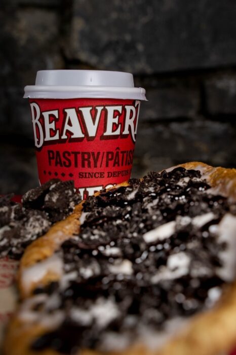 A cup of coffee next to a beavertail pastry topped with Oreo crumbs, a common stop on an Ottawa food tour