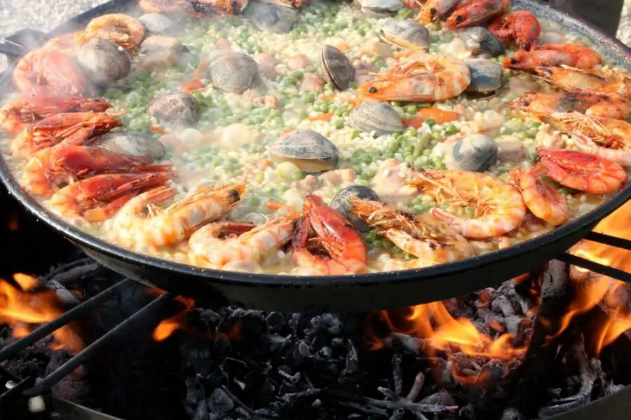 A steel pan filled with shrimp, clams, peas, and other ingredients for paella, a dish that you’ll learn to cook in a Seville cooking class.