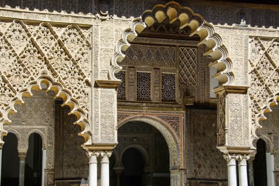 The intricate, cloud-like cream arches of the Royal Alcazar of Seville in the sun.